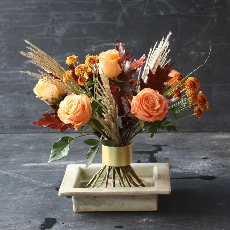 Herbstliches Ikebana-Arrangement mit orangefarbenen Rosen und saisonalem Laub unter Verwendung eines Hanataba Champagne Gold Spiralstielhalters.