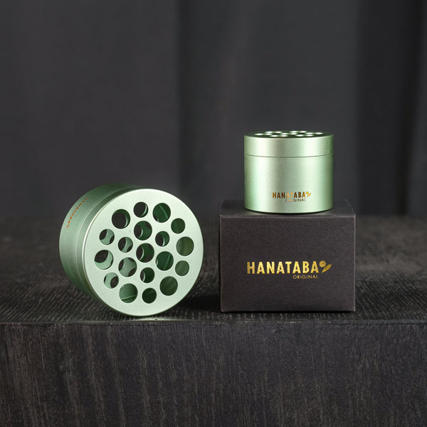 Zwei Hanataba Bouquet Twisters im Matcha Green Design. Die Produkte befinden sich in ihrer schwarzen Originalverpackung mit der goldenen Aufschrift Hanataba Original. Die Auslage befindet sich in einem dunklen Raum auf einem schwarzen Holztisch.