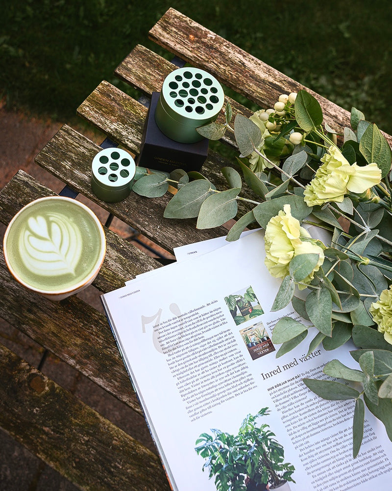 Eukalyptus und eine Tasse Matcha-Tee neben dem Hanataba-Bouquet-Twister auf einem Holztisch in einem Garten.