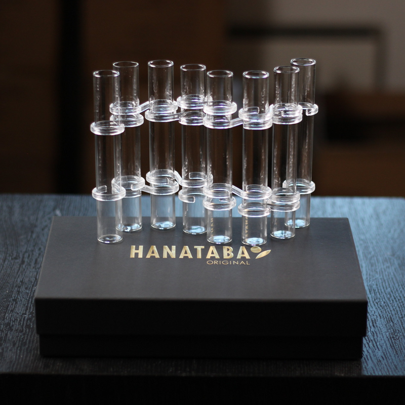 Das Hanataba Original Flower Flute Set wird in einer eleganten schwarzen Schachtel mit goldenem Branding präsentiert und besteht aus einer Reihe von transparenten Glasröhren, die sich für kreative Blumendekorationen eignen.