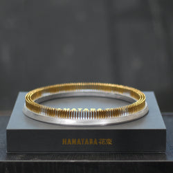 Ein glänzender 200-mm-Kenzan-Ring ruht auf einer eleganten grauen Präsentationsbox mit der goldenen Aufschrift "HANATABA 花束", die Eleganz und Funktionalität in einem Blumenarrangement präsentiert.