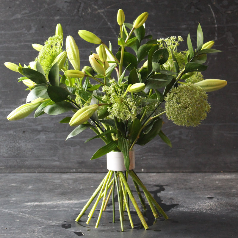 Ein frischer grüner und weißer Blumenstrauß, der mit einem Hanataba Pearly Silver Twister vor einem dunklen Hintergrund gebunden ist.