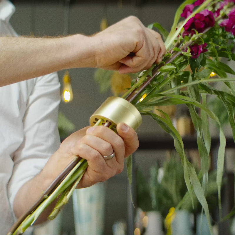 Die Hände eines Mannes montieren gekonnt ein lebhaftes Blumenarrangement mit einer Hanataba Champagne Gold.